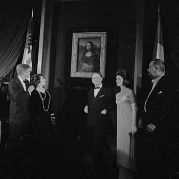 Black and white photo of President and First Lady Kennedy, Vice President Johnson, another man, and another woman dressed in formal attire and standing in front of the Mona Lisa.